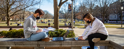 two masked students studying on the quad
