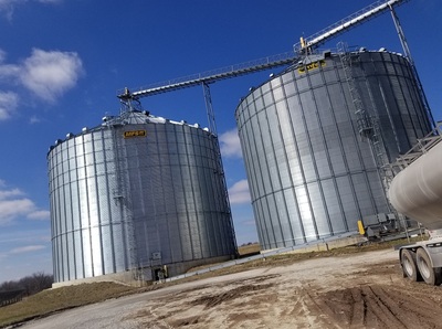 Two large metal grain bins against a bright blue sky
