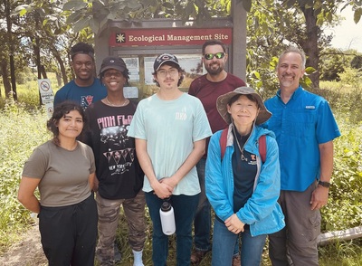 Interns and researchers pose outdoors in front of a wooden sign that says Ecological Management Site