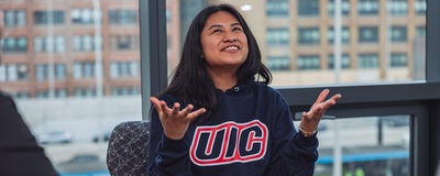 Harumi Barron in University of Illinois Chicago gear spreads her arms in triumph with a cityscape behind her
