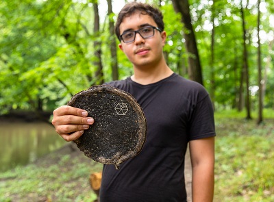 SymmetryWood CEO and founder Gabe Tavas holds up a sample of Pyrus, a wood proxy, in a green wooded area