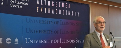 University of Illinois System President Tim Killeen at podium in front of Altogether Extraordinary banner
