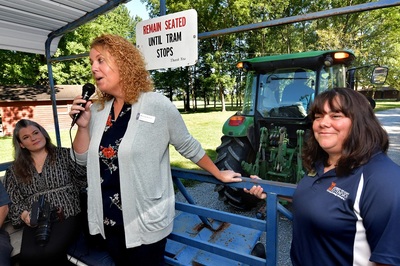 Melissa Wilson speaks via microphone to unseen tour participants as Bronwyn Aly looks on with tractor pulling the tour wagon in the background
