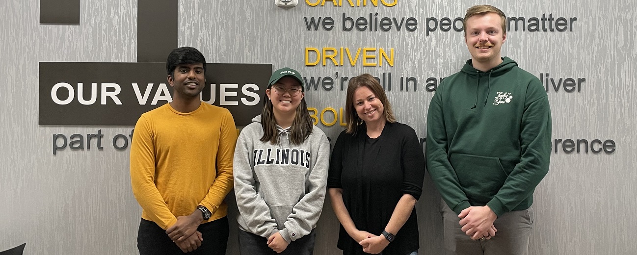 Two Synchrony interns and two employees pose in front of an inspirational sign that says driven